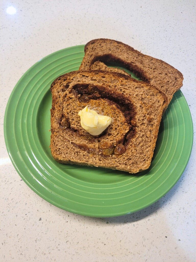 Fresh Milled Sourdough Cinnamon Raisin Swirl Bread on Plate two slices of fresh milled sourdough cinnamon raisin swirl bread on a green plate with butter on top