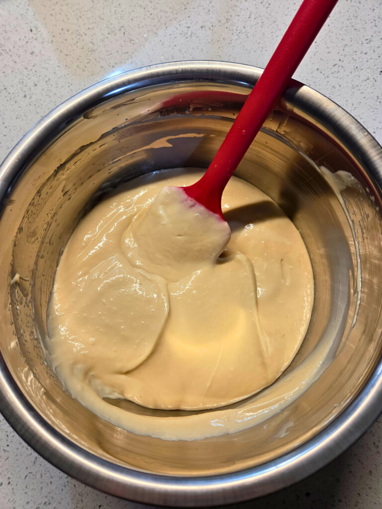 All Mixed with No Lumps bowl of smooth cream cheese icing with a red spatula