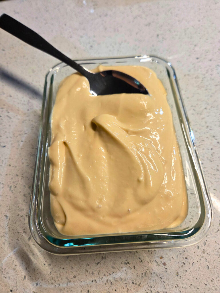 Cream Cheese Icing Ready to Serve Glass container of cream cheese icing with a spoon