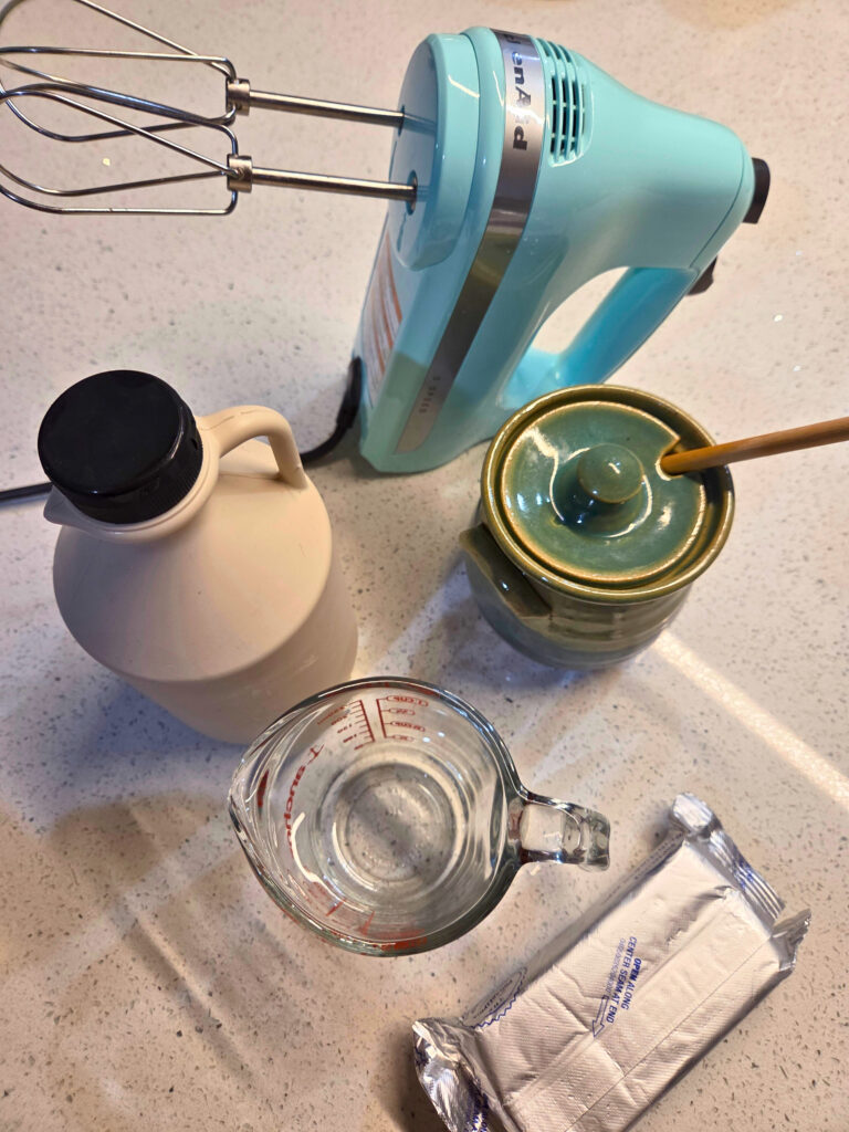 Ingredients for Cream Cheese Icing a block of cream cheese, a jar of honey, a bottle of maple syrup, a liquid measuring cup, and a hand mixer
