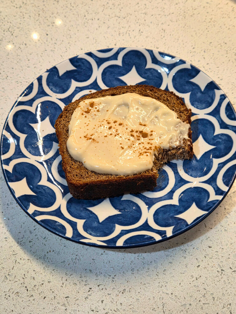Sourdough Autumn Spice Bread piece of sourdough autumn spice bread on a plate covered in cream cheese with a bite taken out of it