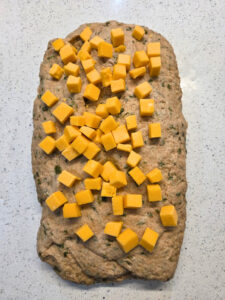 a flattened piece of dough with cheese cubes all over the tops