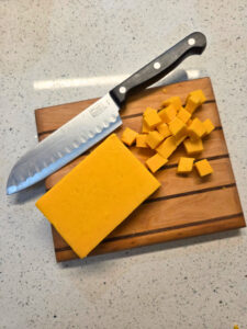 a block of cheese partially cut up into cubes on a cutting board with a knife