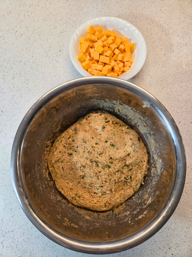 Dough Ready for Shaping - - Sourdough Cheddar and Chive Bread.jpg a ball of sourdough cheddar and chive bread dough next to a bowl of cheese cubes