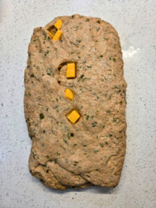 a flattened piece of dough with cheese cubes sticking out from inside