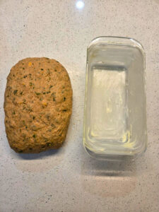 a shaped lump of dough next to a buttered loaf pan