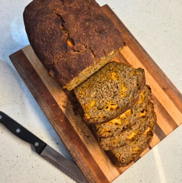a partially sliced loaf of bread on a cutting board, next to a bread knife