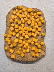 a flattened piece of dough with cheese cubes all over the top