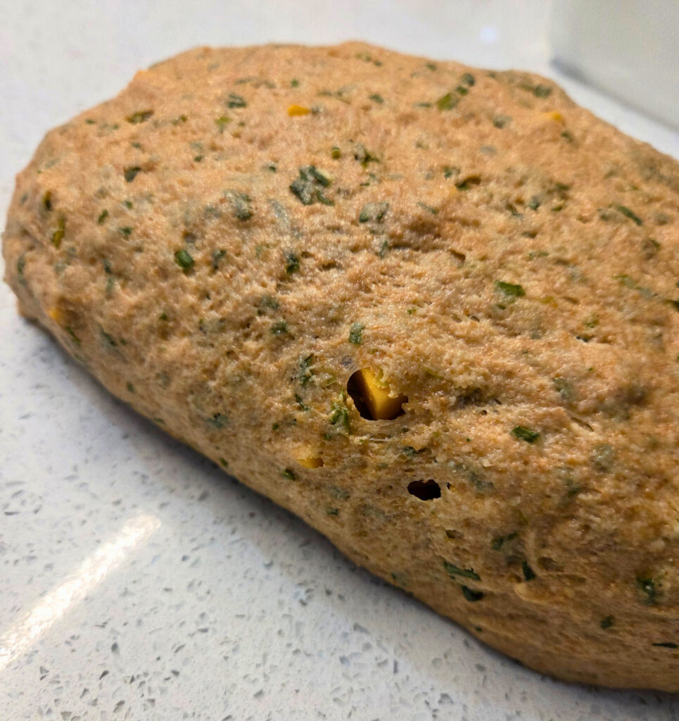 There may be Holes in the Dough - Sourdough Cheddar and Chive Bread.jpg close up of a loaf of dough with chives and holes with cheese cubes poking out